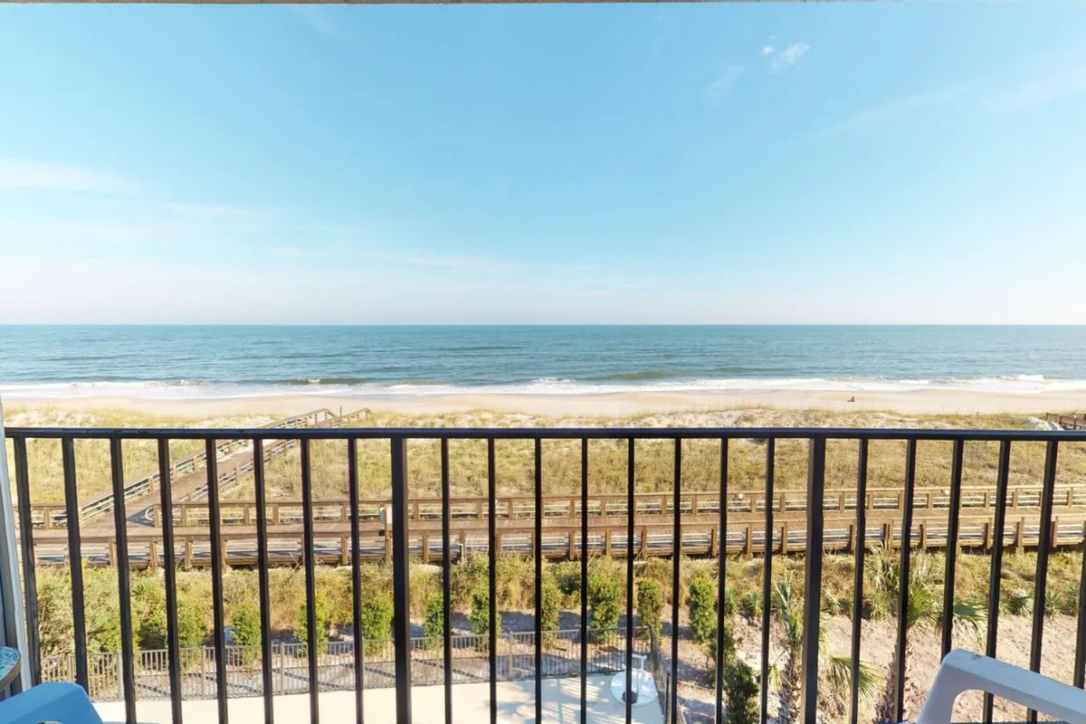 A tranquil ocean view from a balcony, overlooking the beach, railway, and surrounding greenery. The atmosphere is serene yet inviting, hinting at the option to relax together before heading out to explore.