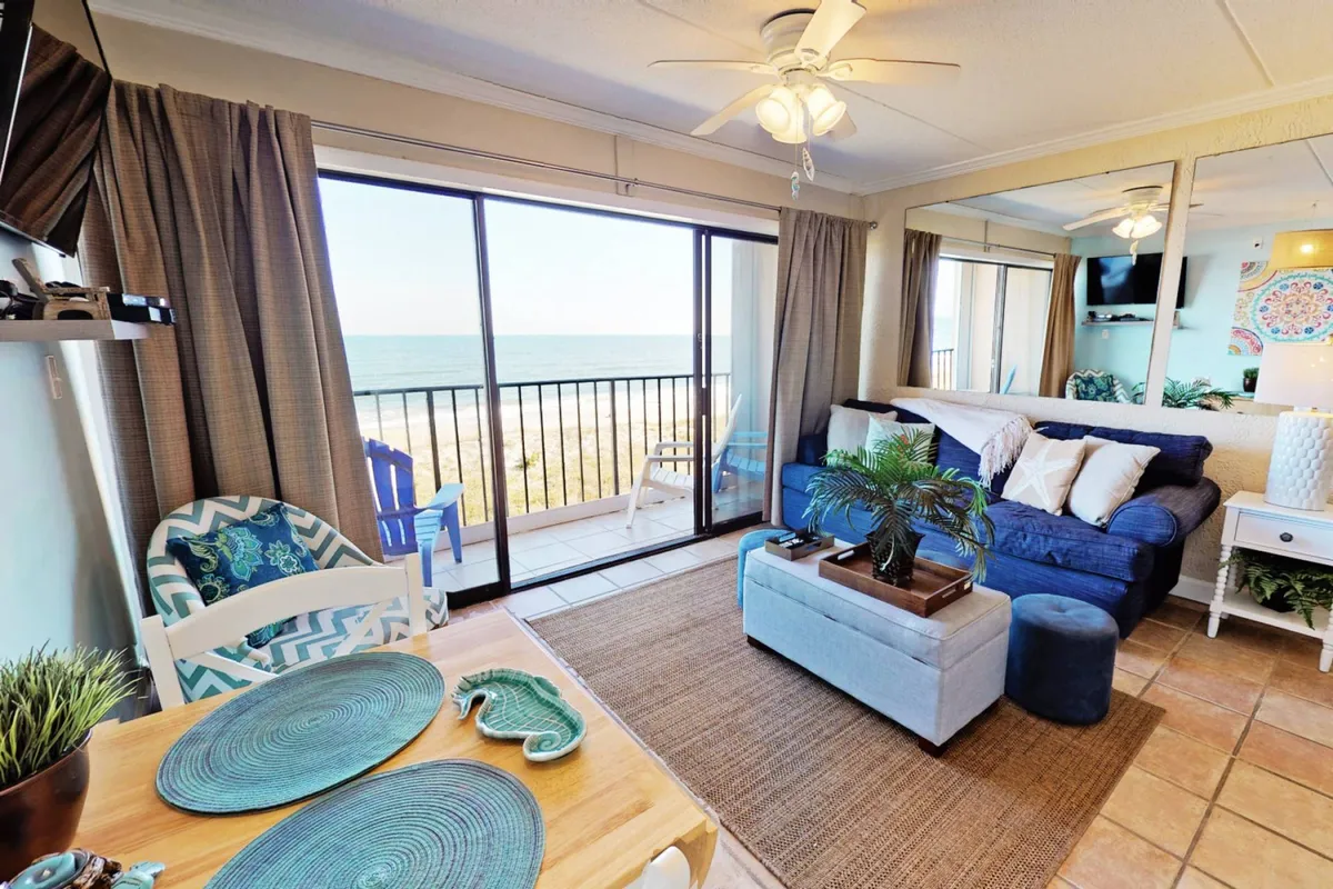 An open-concept living and dining area with a tranquil blue sofa, stylish dining table set with decorative plates, and expansive windows framing a breathtaking ocean view. The space feels inviting and social, perfectly blending comfort with a coastal ambiance.