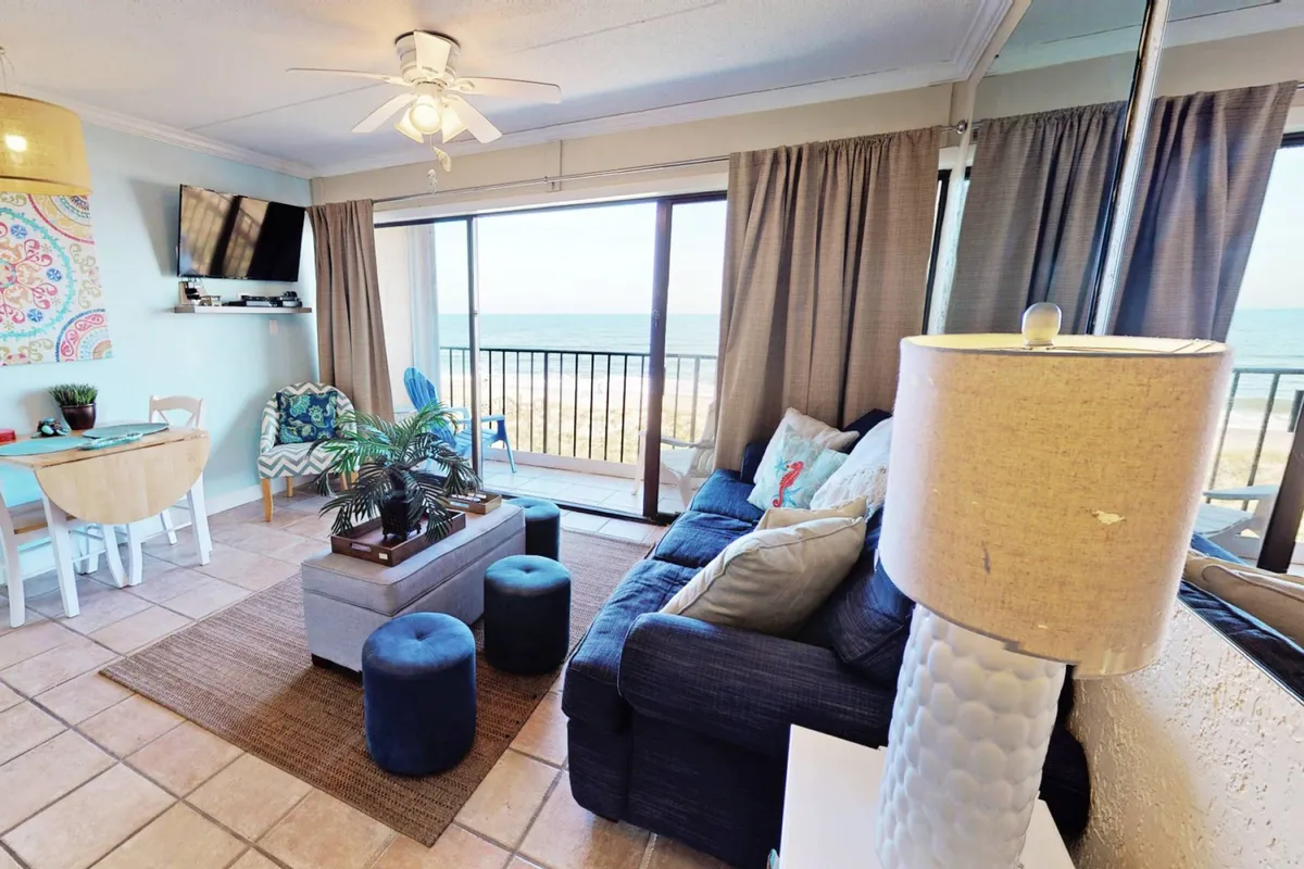 A cozy living area featuring a comfortable sectional sofa facing large windows that offer panoramic ocean views. The adjacent dining area is visible, creating a seamless flow between spaces for relaxation, dining, and socializing.