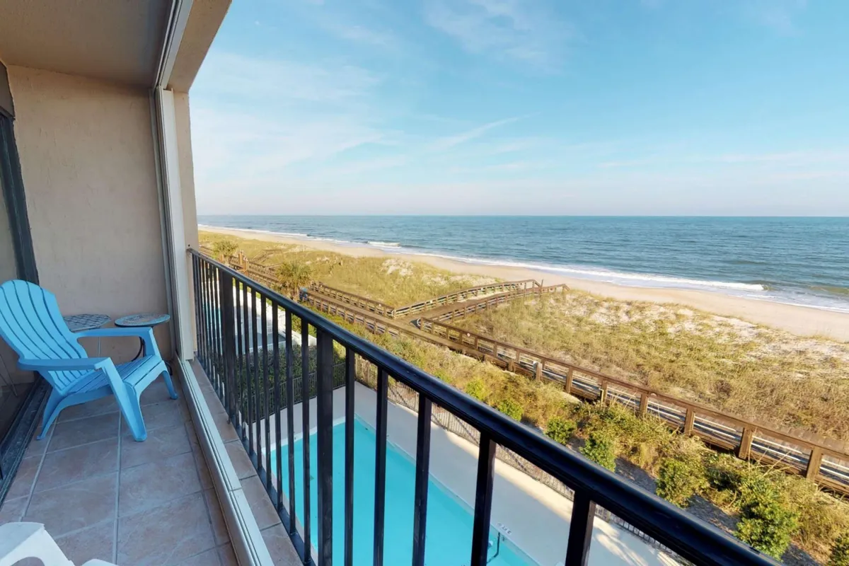 A tranquil exterior shot showcasing an oceanfront balcony with lounge chairs, overlooking the sandy beach and the shimmering ocean. The scene suggests a peaceful morning or twilight moment, inviting viewers to imagine enjoying coffee or cocktails while taking in the view, with a swimming pool also visible for added leisure options.