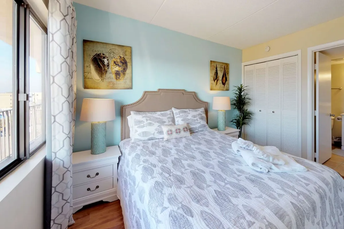 A calming bedroom space with a comfortable bed, tasteful art pieces, and soft lamp lighting. Nightstands and curtains complete the serene environment, inviting peaceful moments at the end of the day.